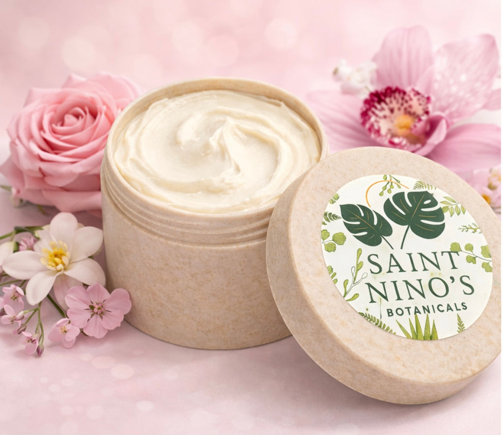 Open Saint Nino’s Botanicals body butter jar showing whipped cream texture beside matching lid on a pink floral background