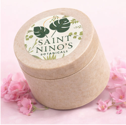 Saint Nino’s Botanicals body butter jar in speckled beige container displayed on pink background with soft floral accents