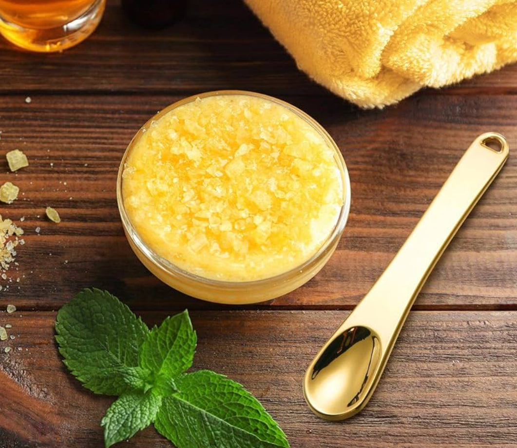 Yellow granulated substance in a glass bowl on a wooden surface with a gold spoon and mint leaves.