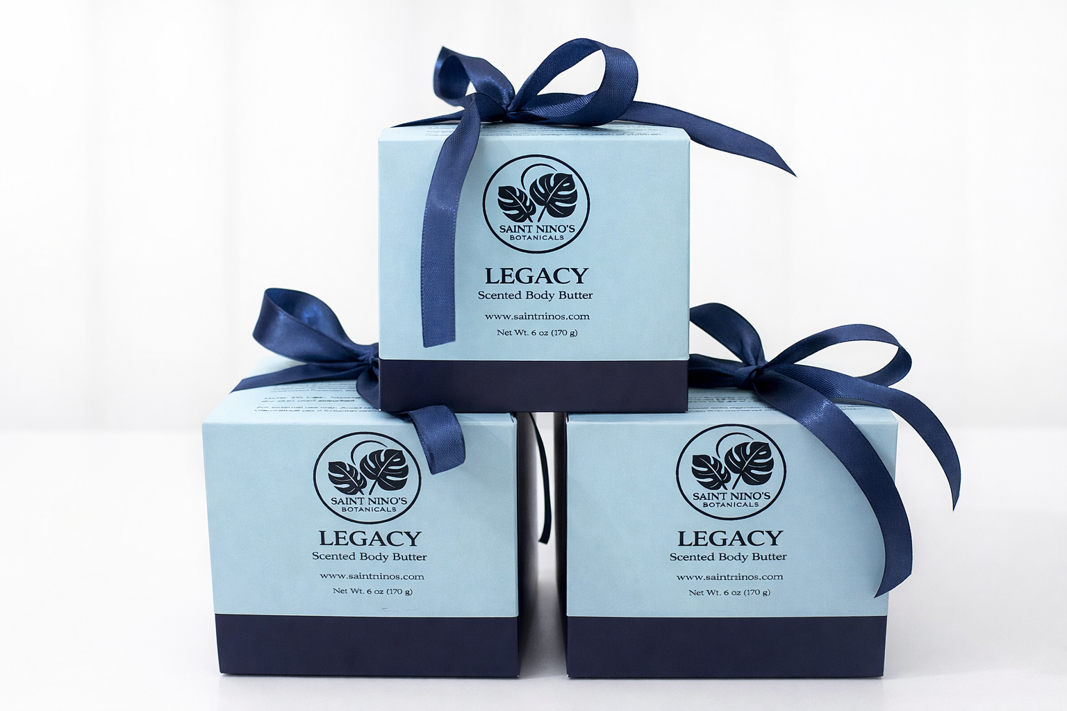 Three boxes of 'Legacy' scented body butter with blue ribbons on a white background